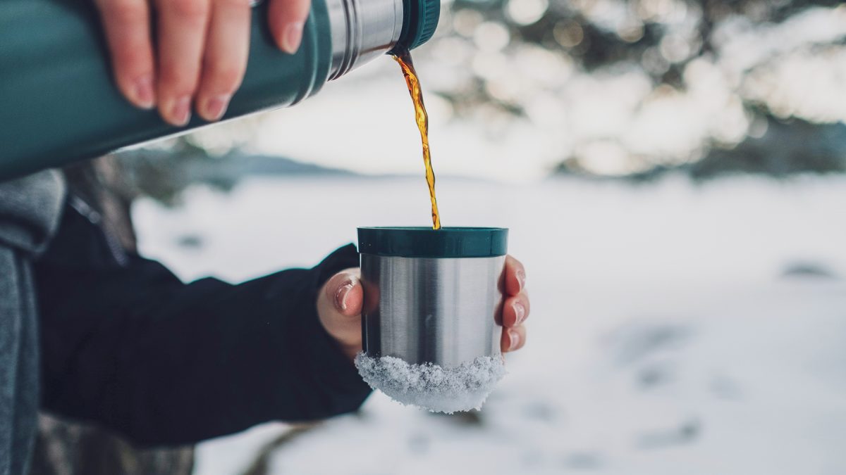 En kvinna häller upp kaffe i en kopp från en termos.