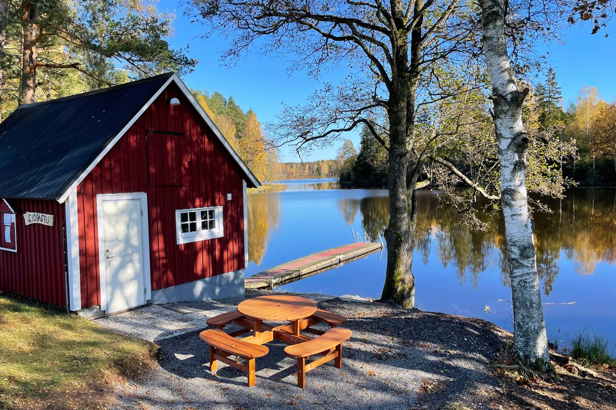En röd bastustuga med ett picknickbord och utsikt över Eseredssjön.