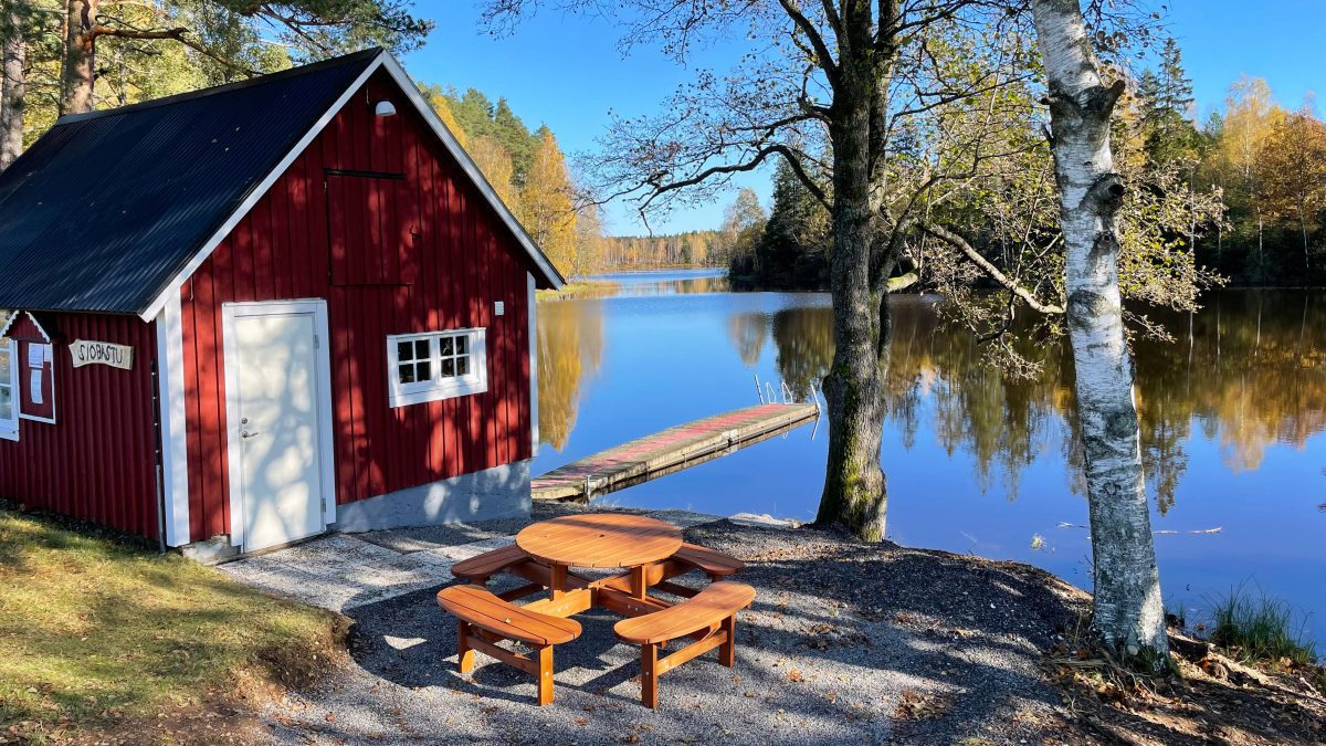 En röd bastustuga med ett picknickbord och utsikt över Eseredssjön.